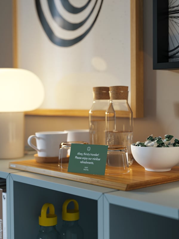 Two clear glass IKEA 365+ carafes with stoppers, white mugs, glasses and a candy bowl on a cutting board on EKET cabinets.