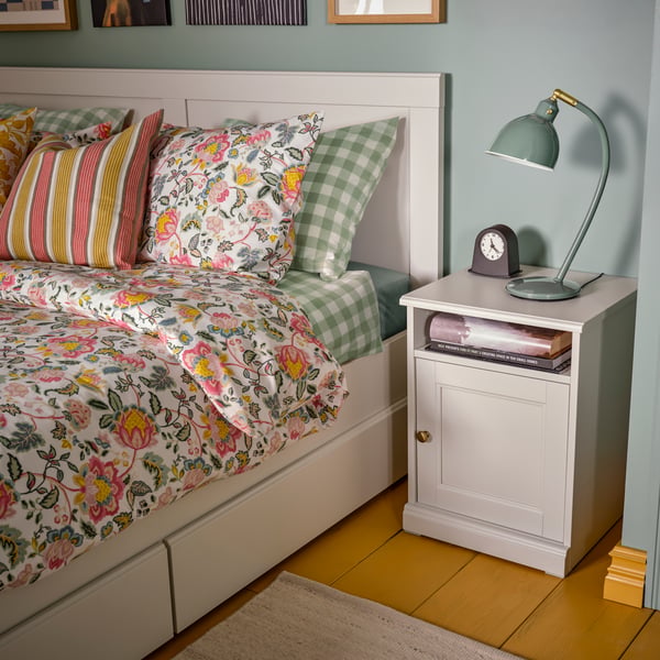 A bedroom with a FÅGELFJÄLLET bedside table and double bed dressed in multicolour/floral pattern DAGGSALVIA bed linen.