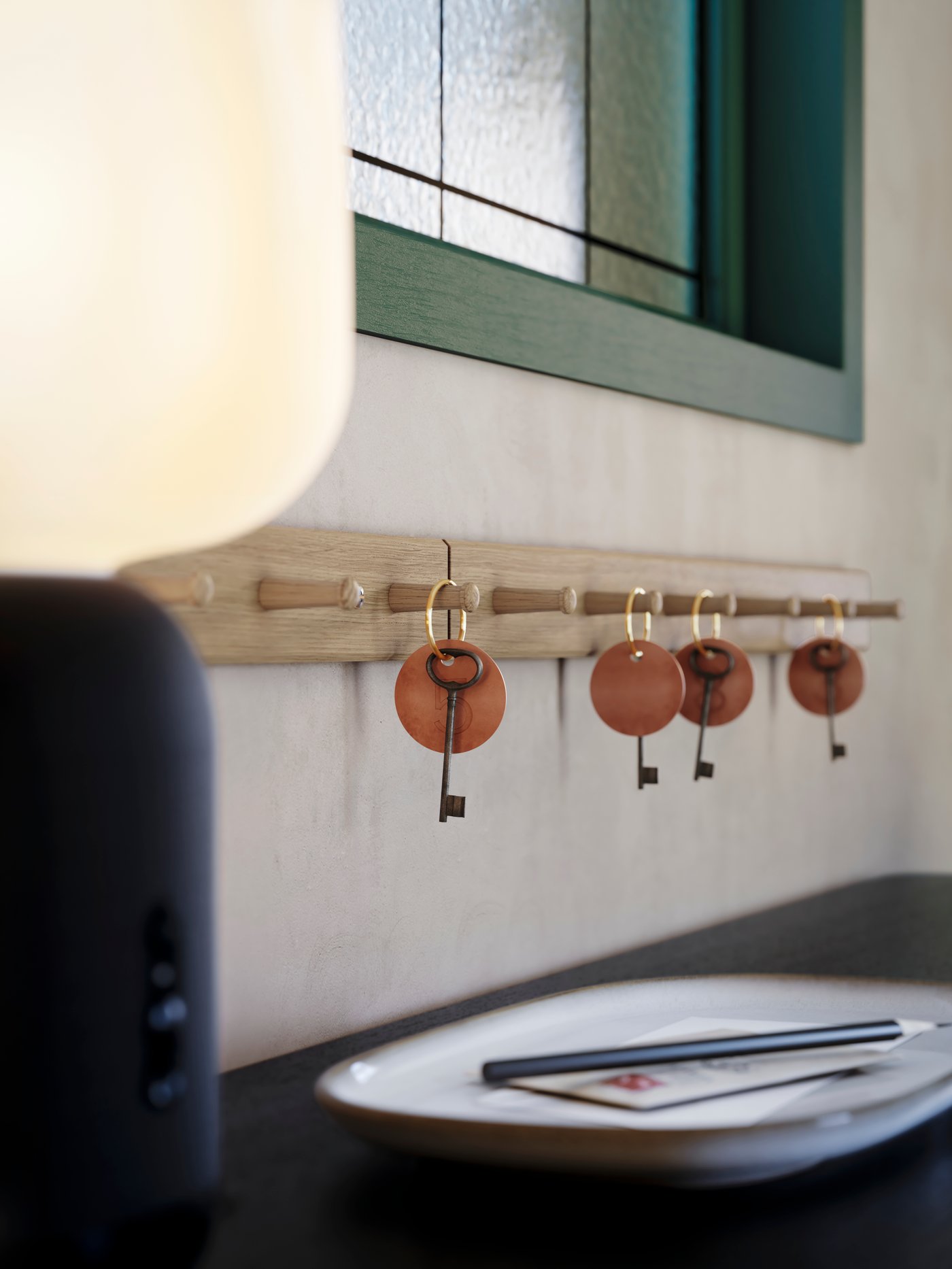 A hotel reception with a gray GLADELIG plate next to a SYMFONISK lamp, a wooden stand with room keys hanging on the white wall.