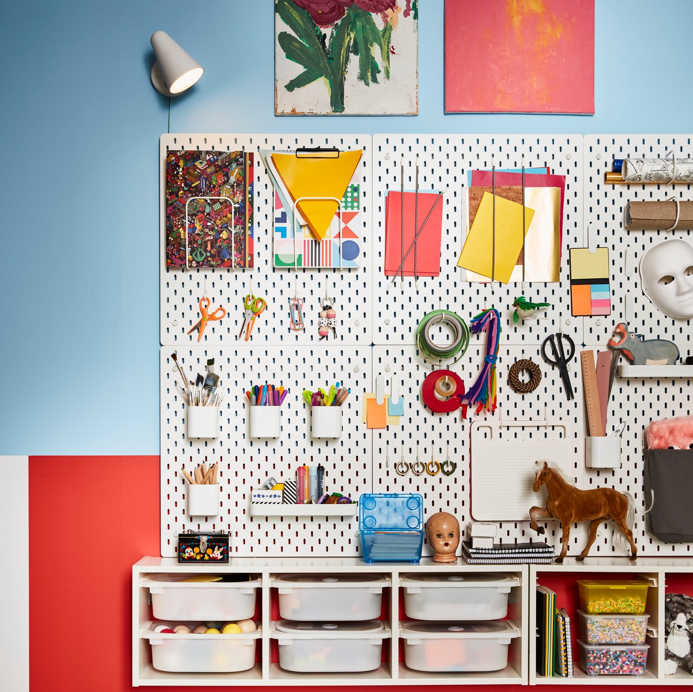 Una parete do colore azzurro appesa alla quale troviamo SKÅDIS pannelli portaoggetti bianchi con molti accessori agganciati. Sotto una combinazazione con contenitori TROFAST.