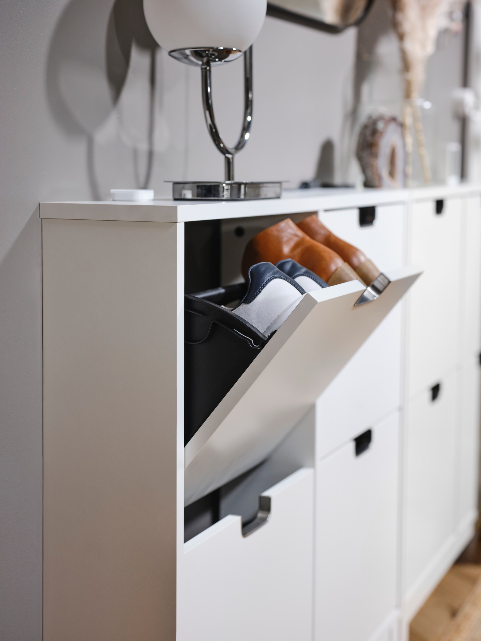 Krupan kadar kompaktnog belog zidnog elementa za odlaganje obuće u skandinavskom deko stilu sa stonom lampom na vrhu.