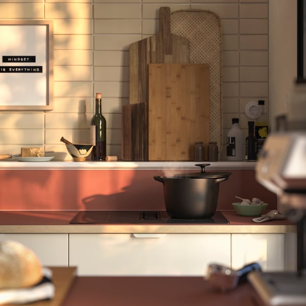 A minimalist kitchen featuring a grey countertop with a black induction hob, a wooden cutting board, and various bottles.
