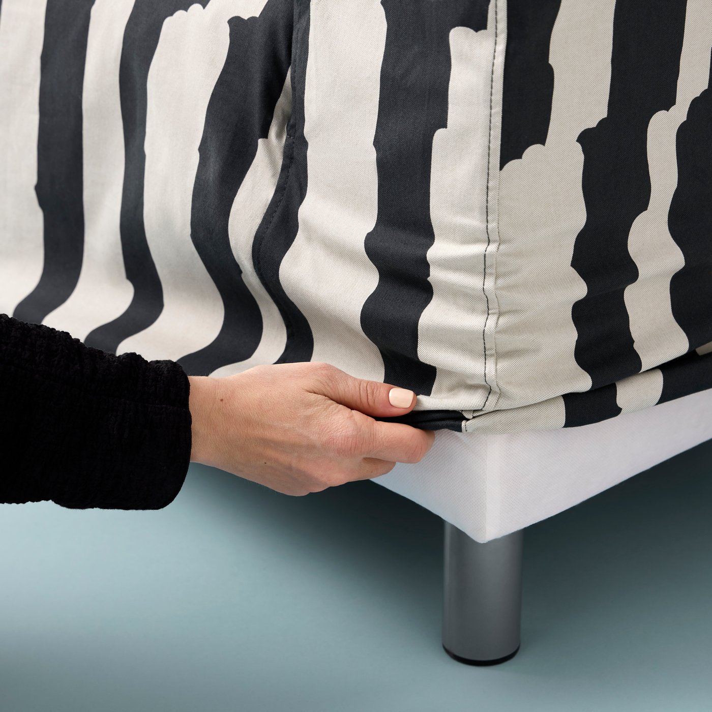 A hand adjusting a lower corner of the cover of a Grimsmåla black-and-white, zebra-stripe KLIPPAN two-seat sofa.