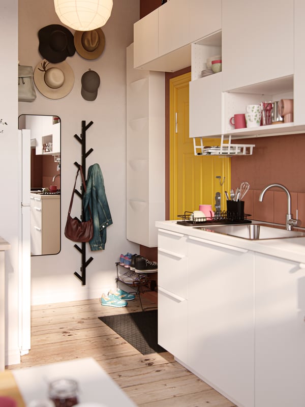 A small hallway with a yellow front door, hats and a bag hang above a wall-mounted clothing rack next to a mirror.