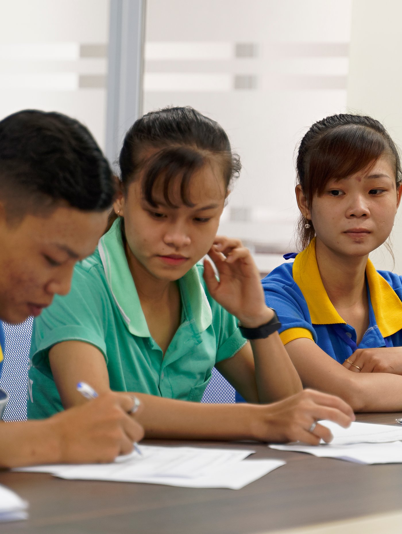 Two people at an IKEA supplier somewhere in Asia sitting at a desk watching as a third person fills in a form.