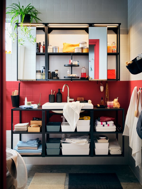 A red-and-white-tiled bathroom with a big ENHET combination with open cabinets, filled with neatly arranged accessories.