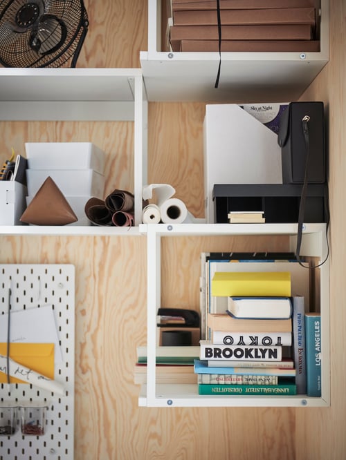 Multiple open shelving units with books and office supplies, and a pegboard mounted on a wood board.