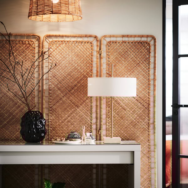 A handmade rattan TOLKNING room divider placed flat against a wall with a white MALM dressing table in front of it.