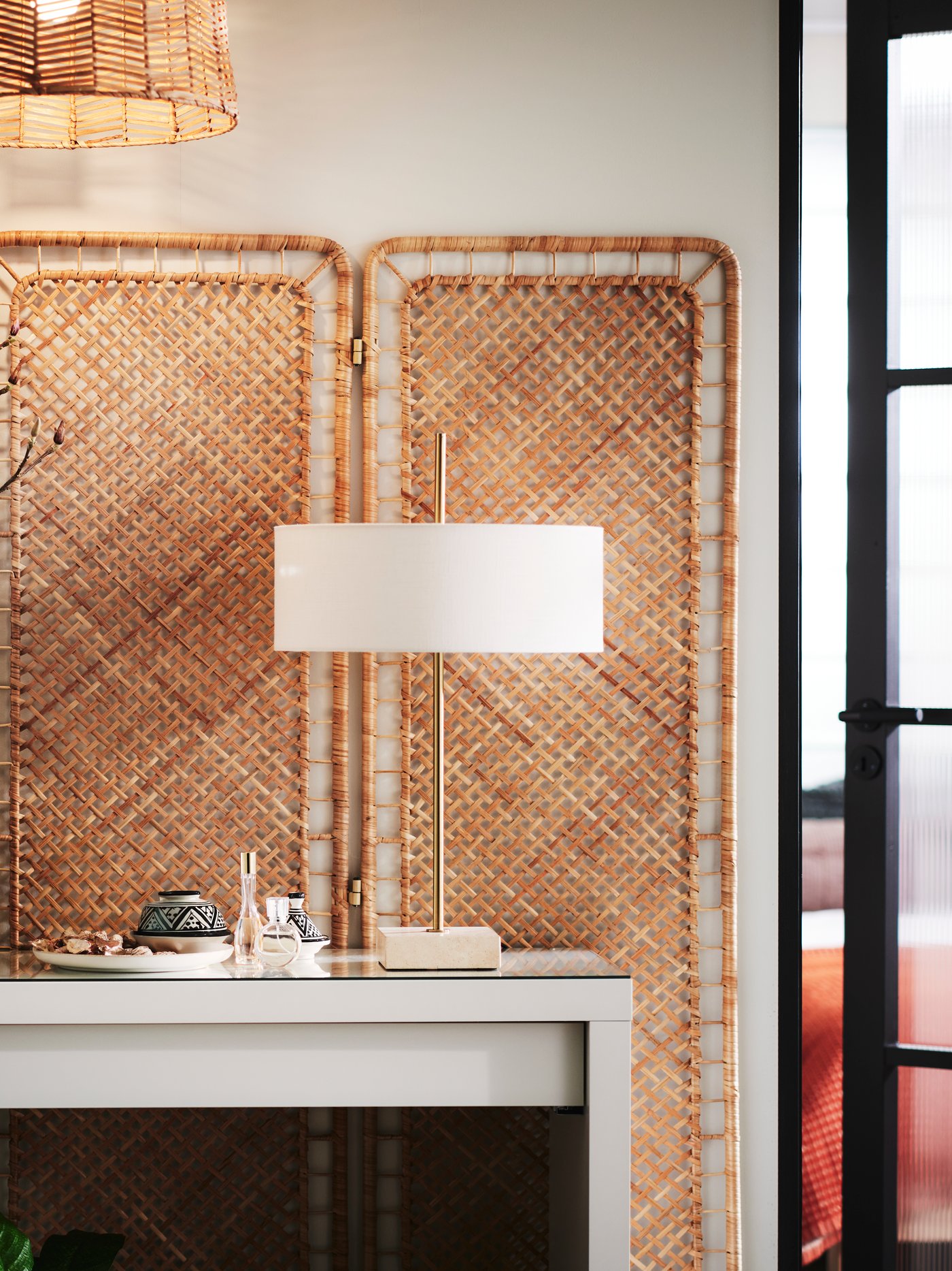 A handmade rattan TOLKNING room divider placed flat against a wall with a white MALM dressing table in front of it.