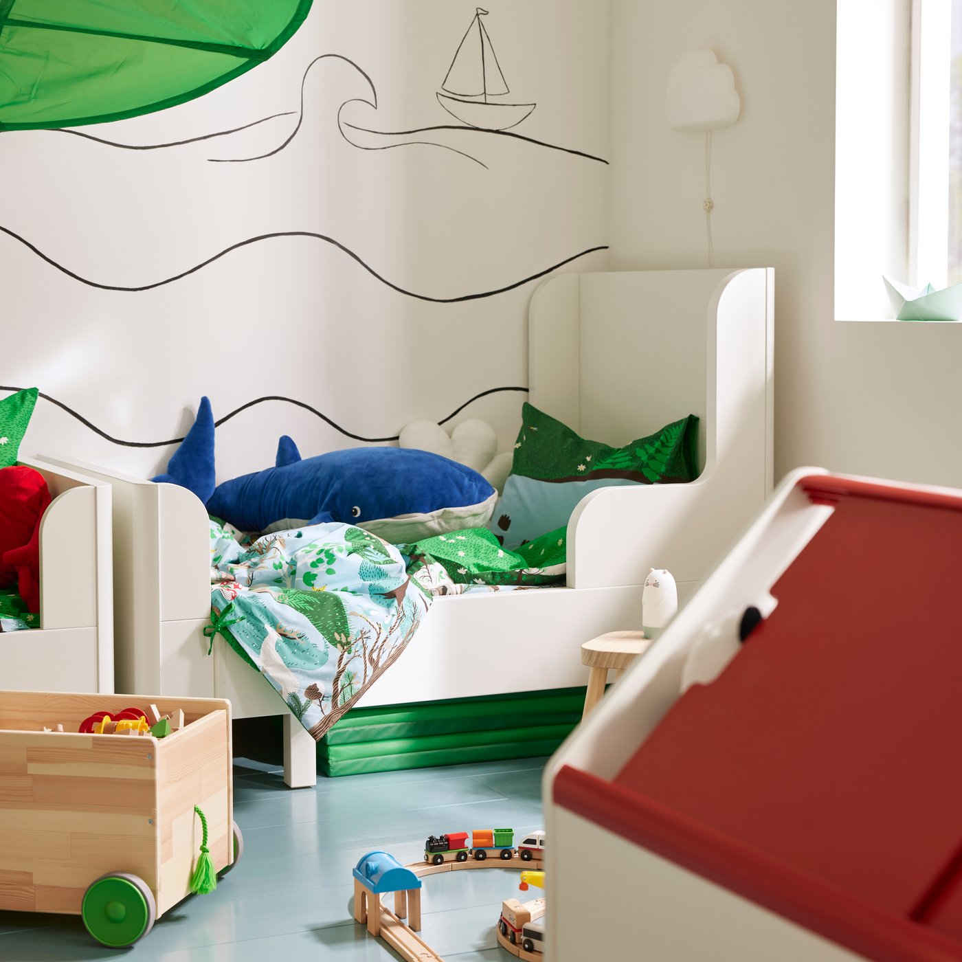 A children’s room in daylight with toys everywhere, a BUSUNGE extendable bed at the back near a FLISAT toy storage on wheels.