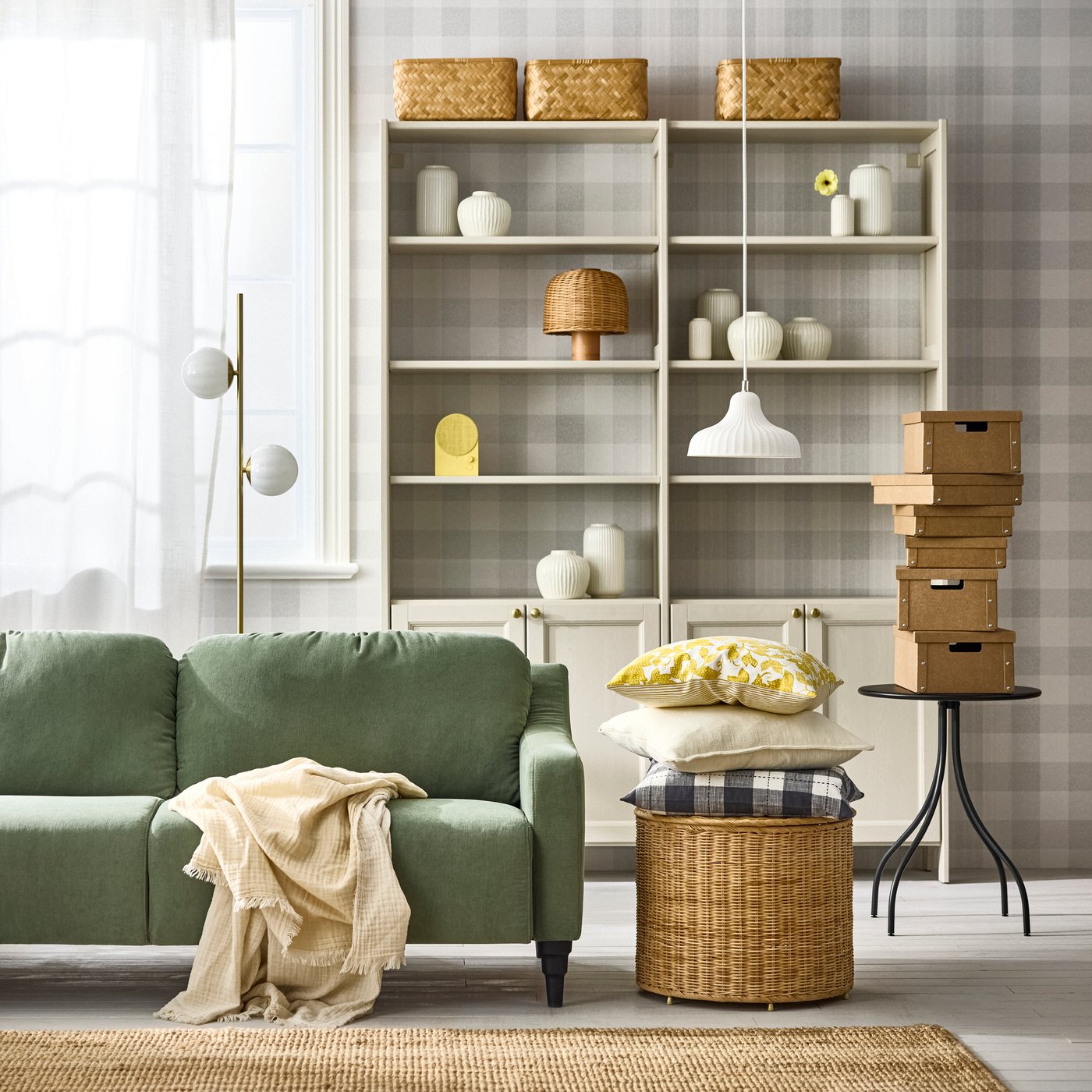 A light space with a beige GULDDRAGARE storage unit with cabinets and shelves, flanked by a sofa, lamps, baskets and boxes.
