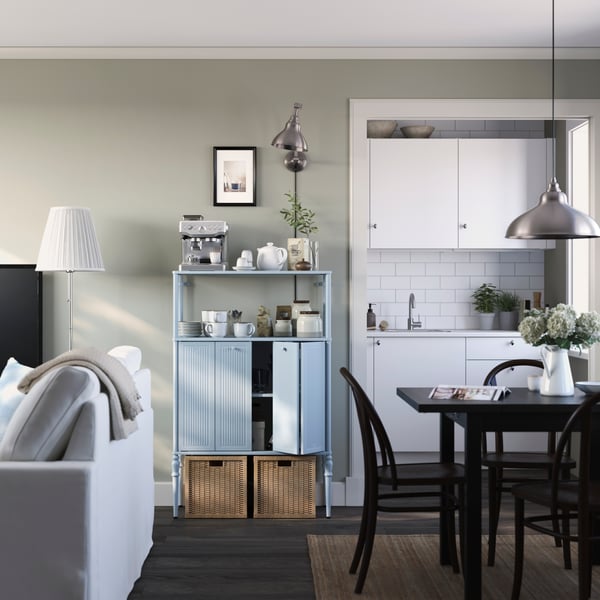 A light room where a SÅGMÄSTARE cabinet laden with coffee accessories is nestled between a sofa and a dining area.