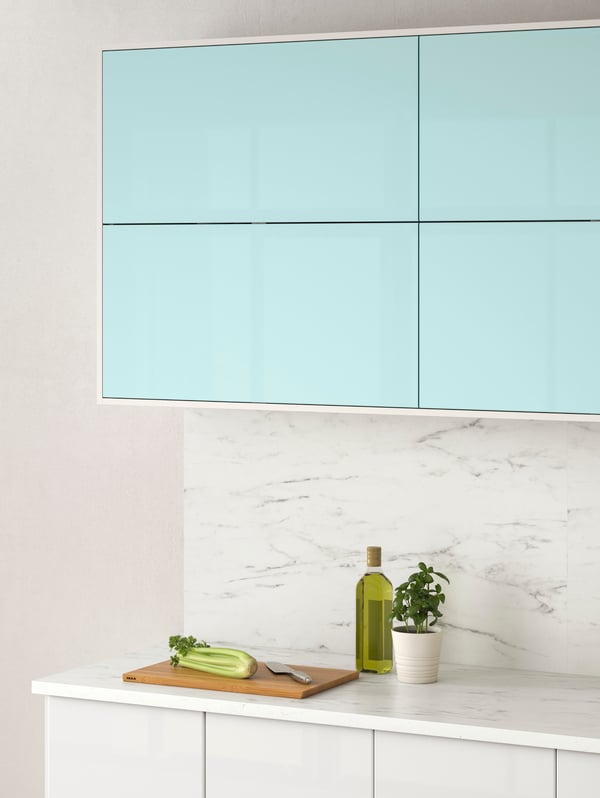 Wall cabinets with JÄRSTA kitchen fronts in light turquoise and various items on an EKBACKEN marble effect laminate worktop.