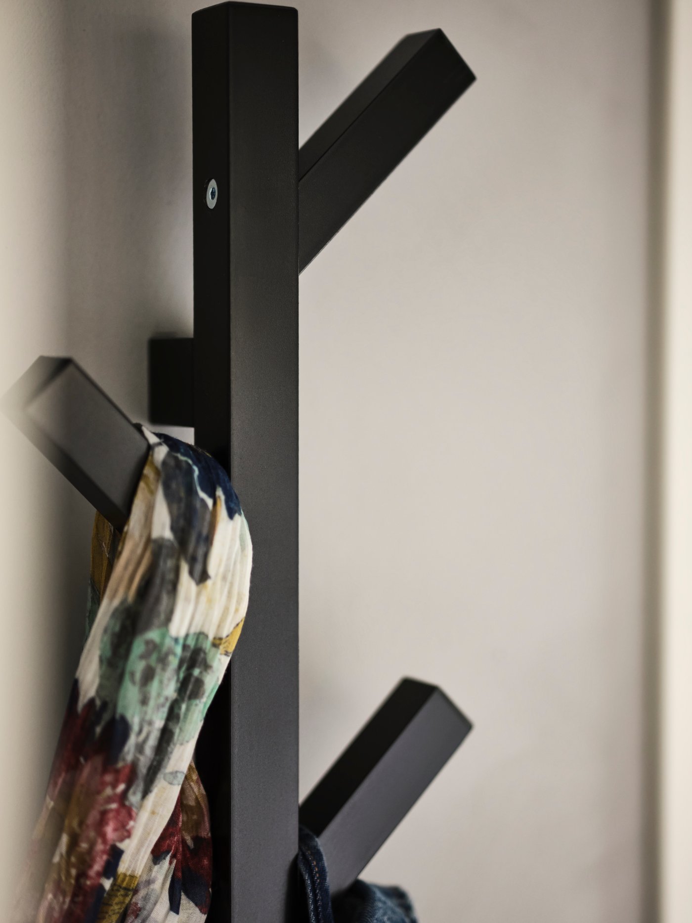 A black TJUSIG hanger attached to a wall with a patterned scarf hanging from it.