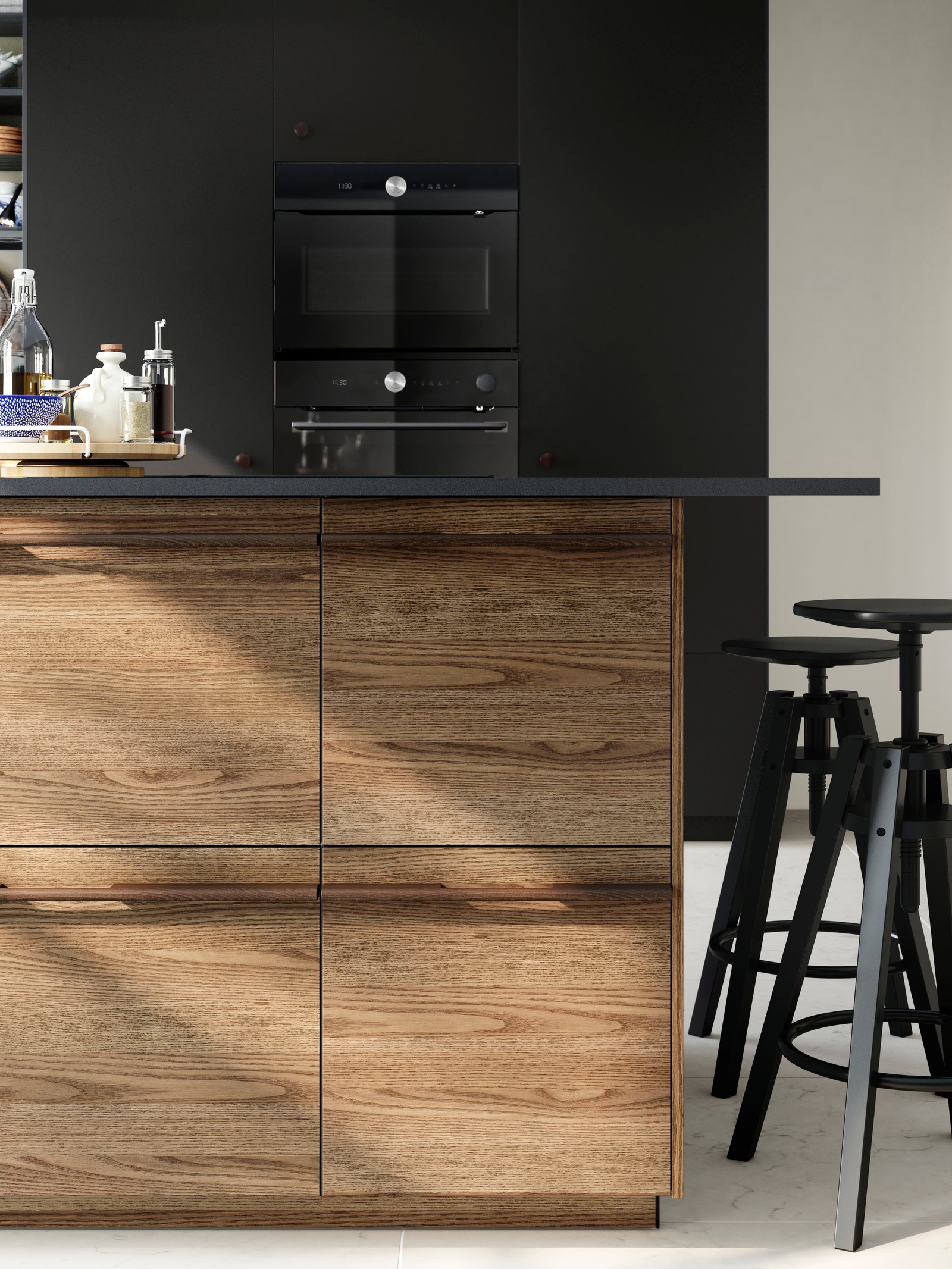 A kitchen with STENSTA dark brown ash veneer drawer fronts, black countertop, and black bar stools, and black appliances in the background.
