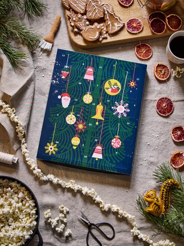 VINTERSAGA adventskalender på et dekket bord med tørkede appelsiner og popkornsnor. 