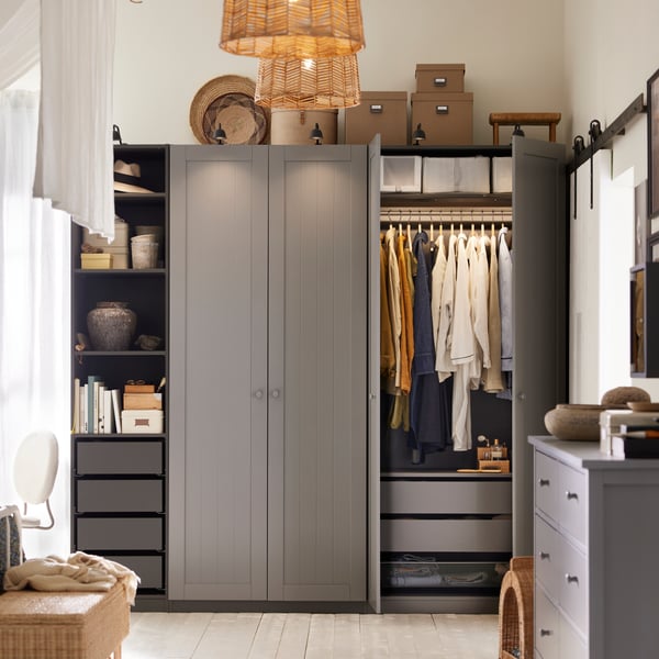 Dormitorio con una combinación de armario PAX/GULLABERG, ropa colgada, cajas en la parte superior y objetos decorativos sobre un estante abierto.