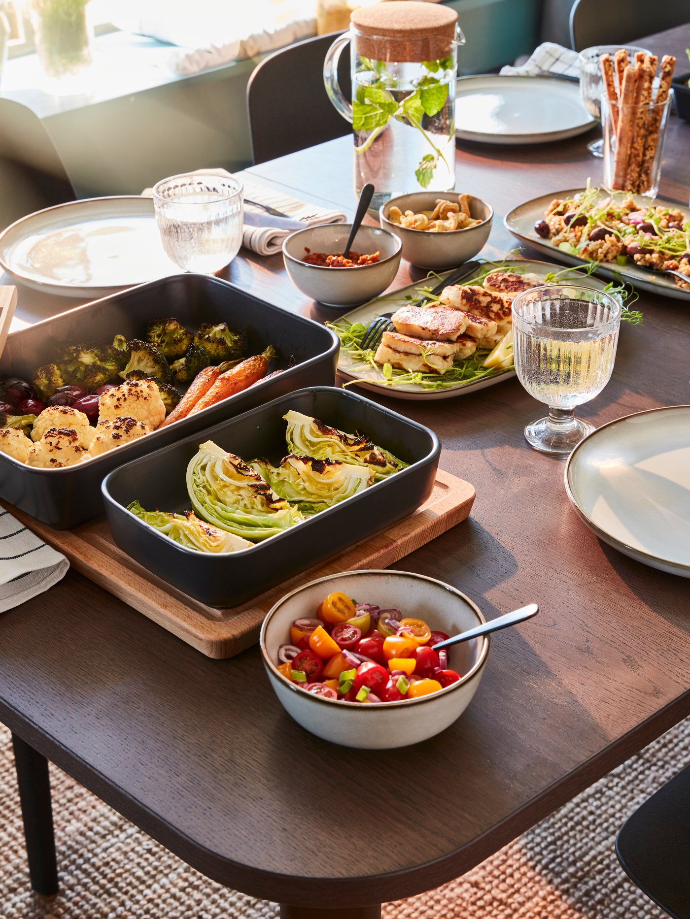 Una mesa extensible en la que hay fuentes para horno con comida, platos, cuencos con comida, copas y una jarra con tapa.