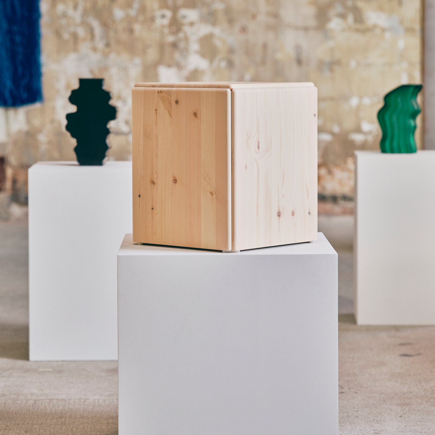 Three objects in wood, glass and ceramics from IKEA KONSTRUNDA art collection in a rough studio setting with concrete walls.