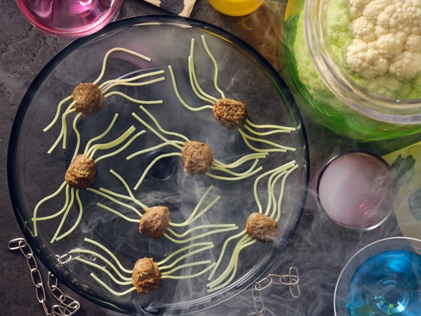Spider meatballs made with HUVUDROLL plant balls or meatballs and spaghetti for legs laid on a black plate with smoke.