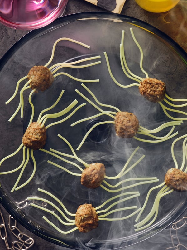 Spider meatballs made with HUVUDROLL plantballs or meatballs and spaghetti for legs laid on a black plate with smoke.