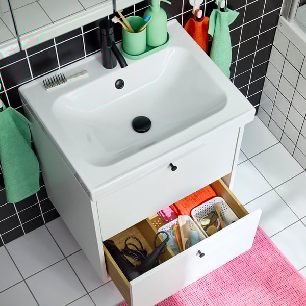 A white HAVBÄCK/ORRSJÖN washstand with two drawers. One is open and inside are small boxes in different sizes. White floor.