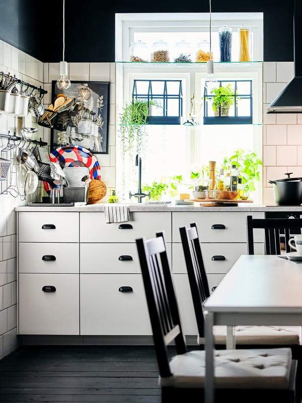 A corner of a black-and-white kitchen with white base cabinets and multiple utensils on rails fitted on a white-tiled wall.