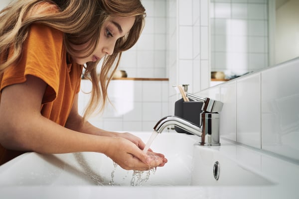 Une fille est penchée au-dessus d'un lavabo dans la salle de bain et se lave les mains sous l'eau courante d'un robinet.