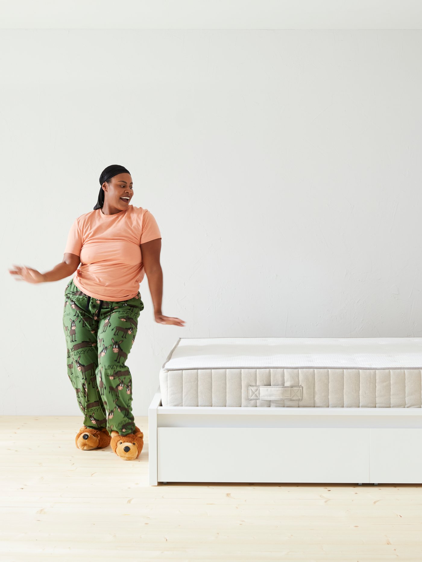 Een vrouw staat naast een onopgemaakt bed en doet een dansje