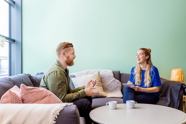Zwei Personen sitzen sich auf einer grauen Couch gegenüber. 