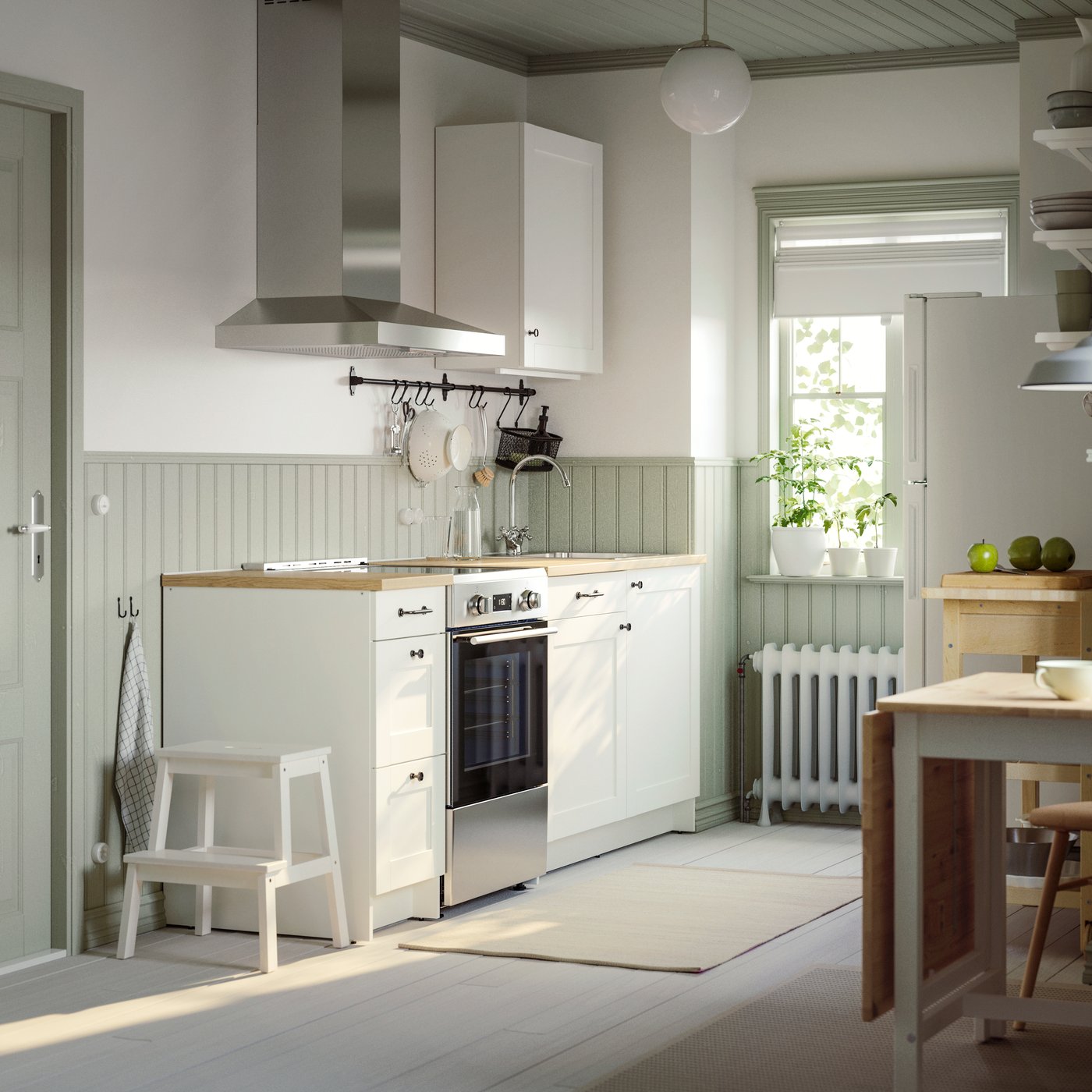 A small, bright kitchen has white KNOXHULT kitchen cabinets and a HULTARP rail with kitchen accessories hanging from hooks.