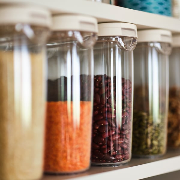 A selection of grains in transparent/white 1.3 l IKEA 365+ dry food jars with lids on a shallow, white shelf.