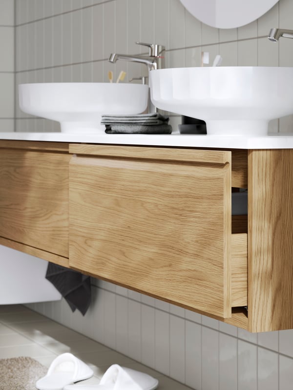 Bathroom featuring the LERSJÖN white countertop wash-basin with chrome fixtures, a wooden vanity, and slippers on the floor.