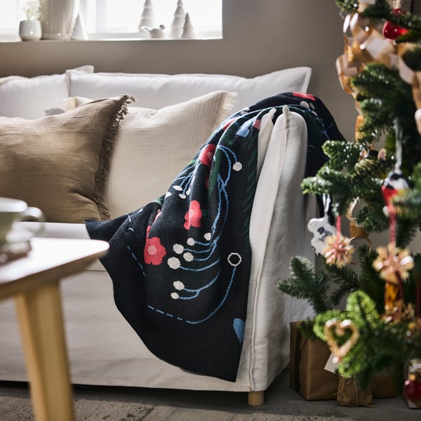 En vit soffa med en julfilt står bredvid en pyntad grön.