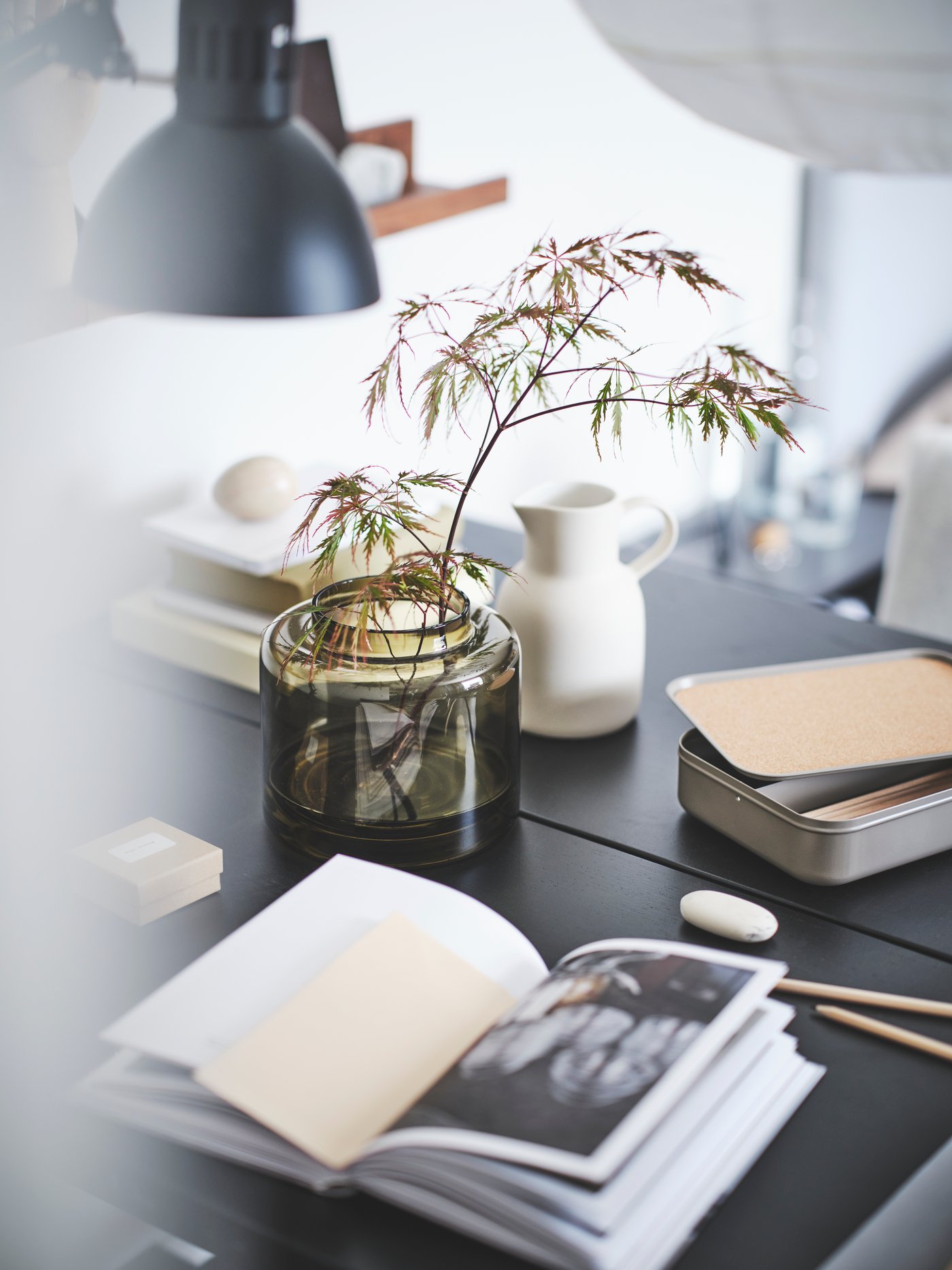 A white SLÄTTIKA jug sits on a table amongst other home decor. 