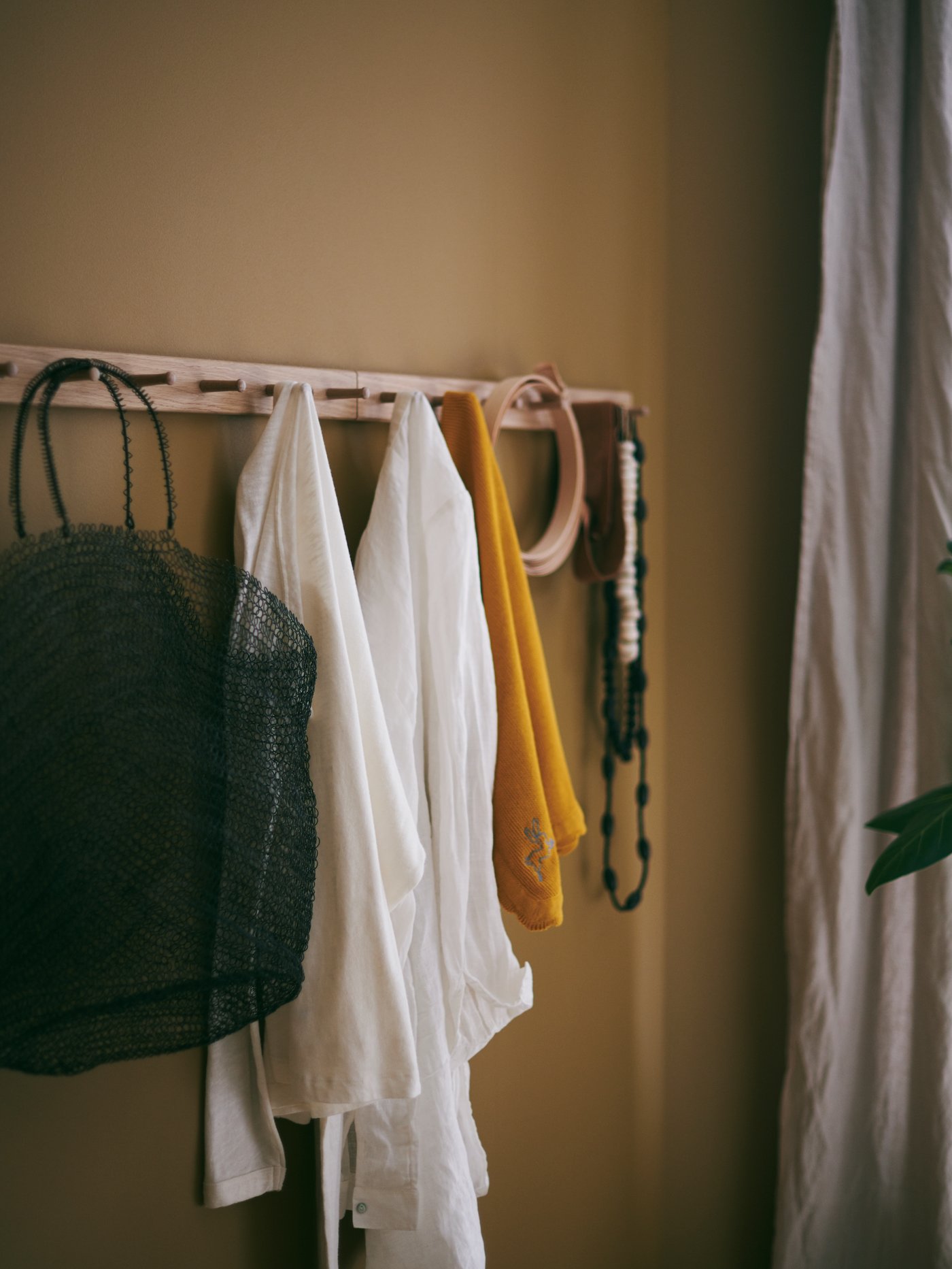Clothes, a bag and various accessories in diverse colours hanging from a HÖVOLM rack with 6 knobs.