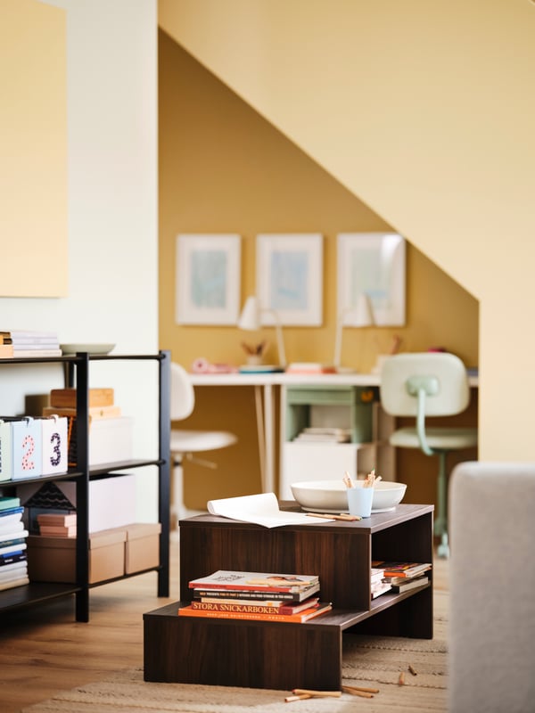 A HOLMERUD coffee table is in the middle of a yellow living room, close by a study nook under the stairs.