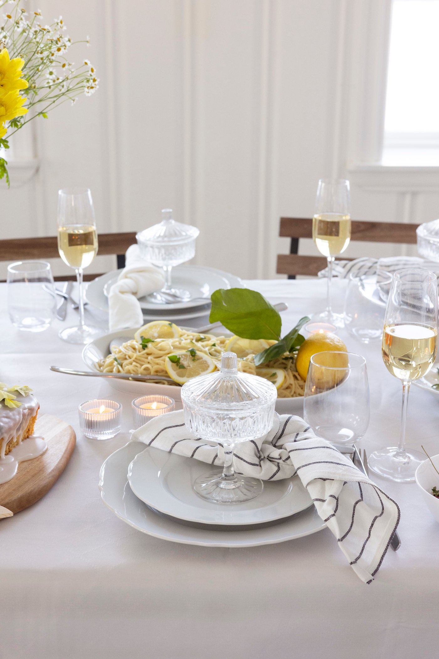 Eleganter, weiss gedeckter Esstisch mit Pastateller, Weingläsern und einer frischen Zitrone als Tischdekoration.