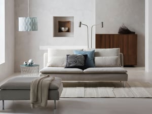 A light SÖDERHAMN sofa with decorative cushions in a minimalist living room with light walls, a wooden cabinet and modern lamps.