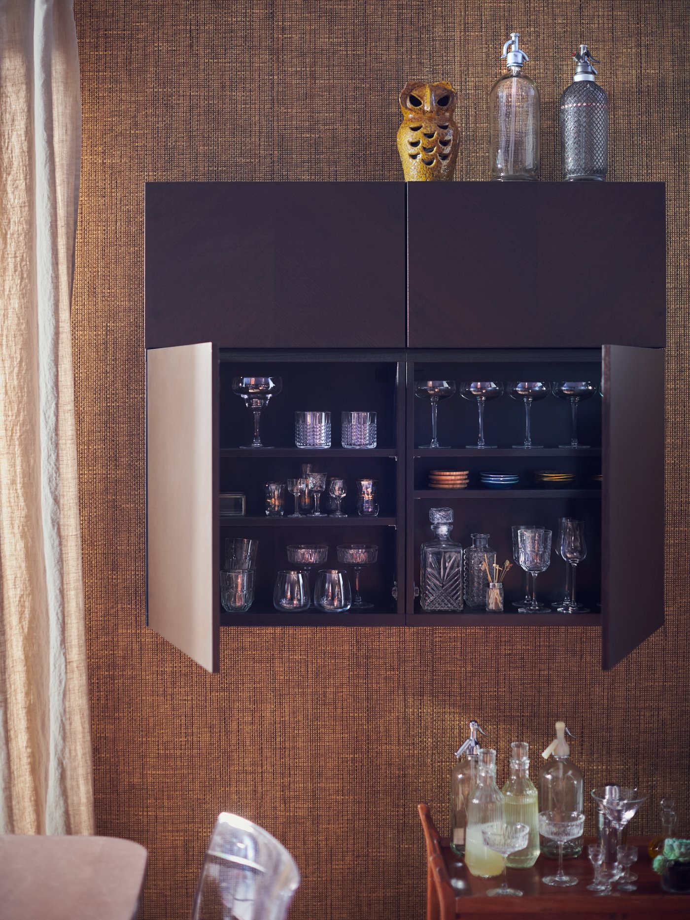 Et væghængt barskab i mørk træfinér på en væg med hessian.