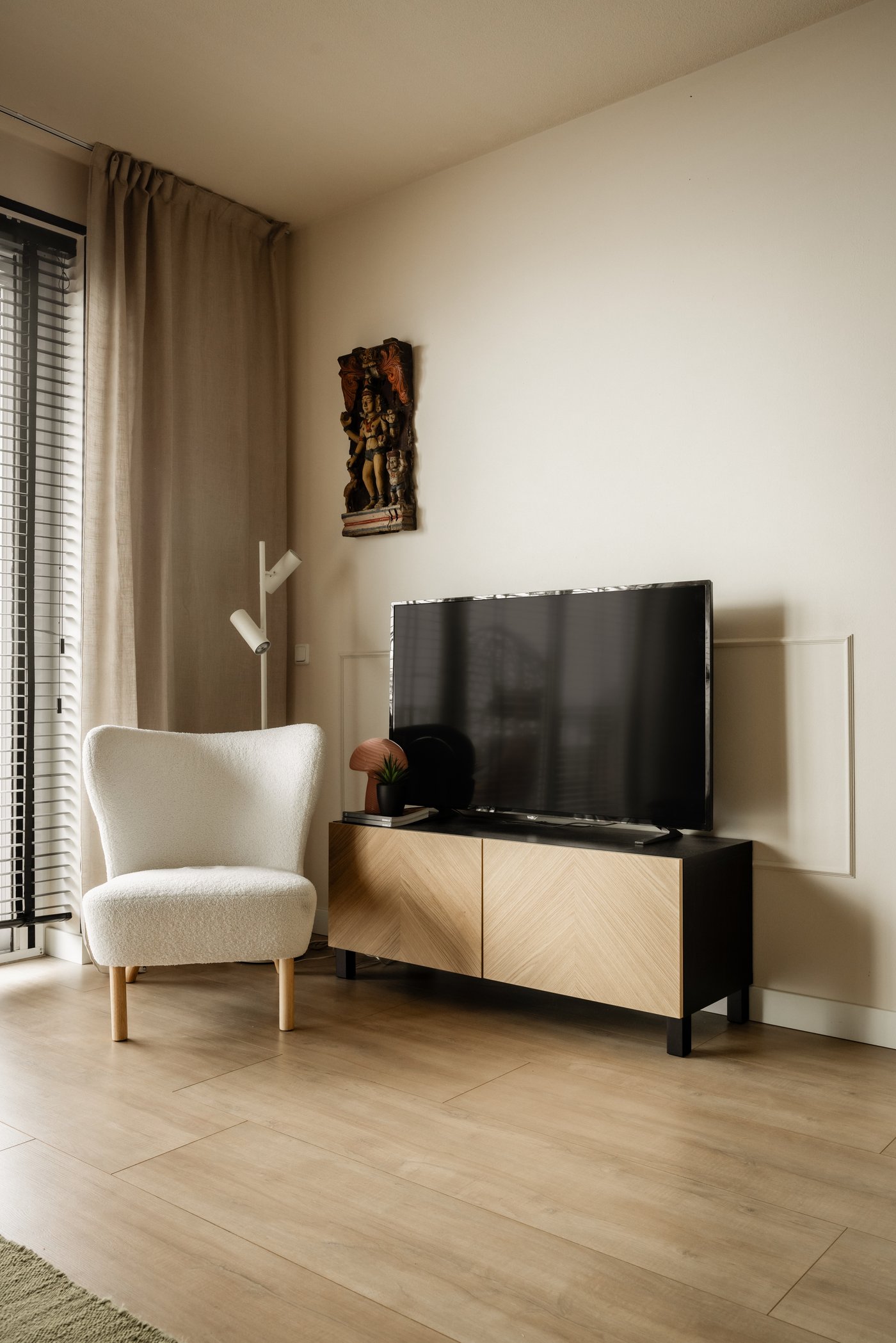 Hoek van de woonkamer met een tv-meubel met daarop een tv. Hiernaast staat een witte fauteuil en een witte vloerlamp.