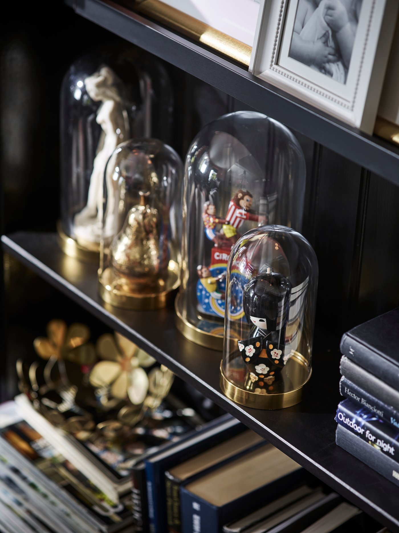 Figurki pod szklanymi kopułami BEGÅVNING na półce czarnego regału.