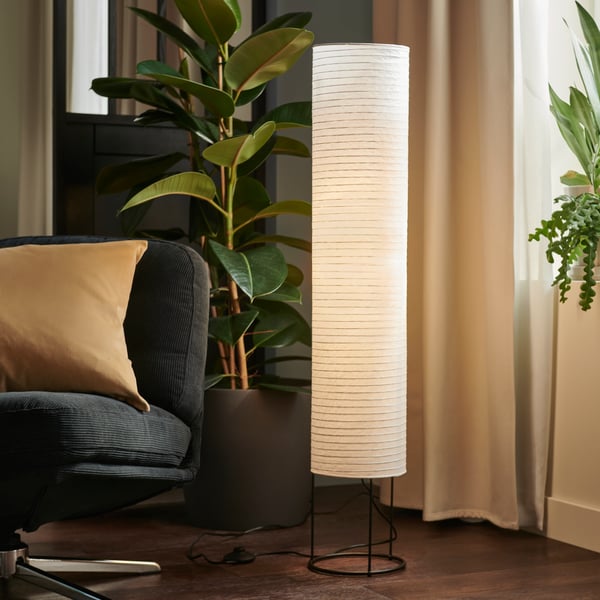 A corner of a living room furnished with a DYVLINGE swivel armchair, a large leafy plant, and a lit STRANDAD floor lamp.