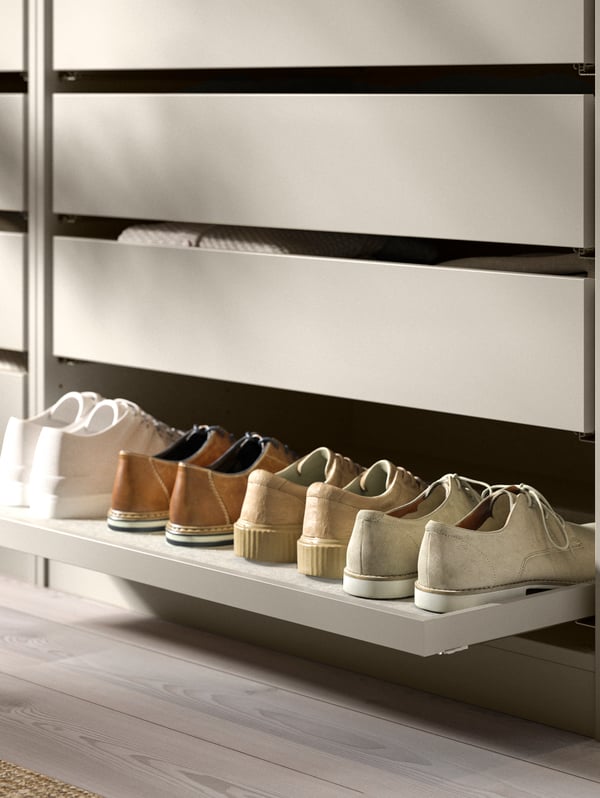 Le bas d’une armoire-penderie PAX dotée d’un plateau coulissant KOMPLEMENT chargé de quatre paires de chaussures.