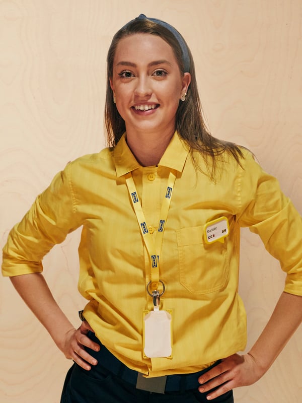 En IKEA medarbetare i en gul skjorta står med  händerna på höfterna.