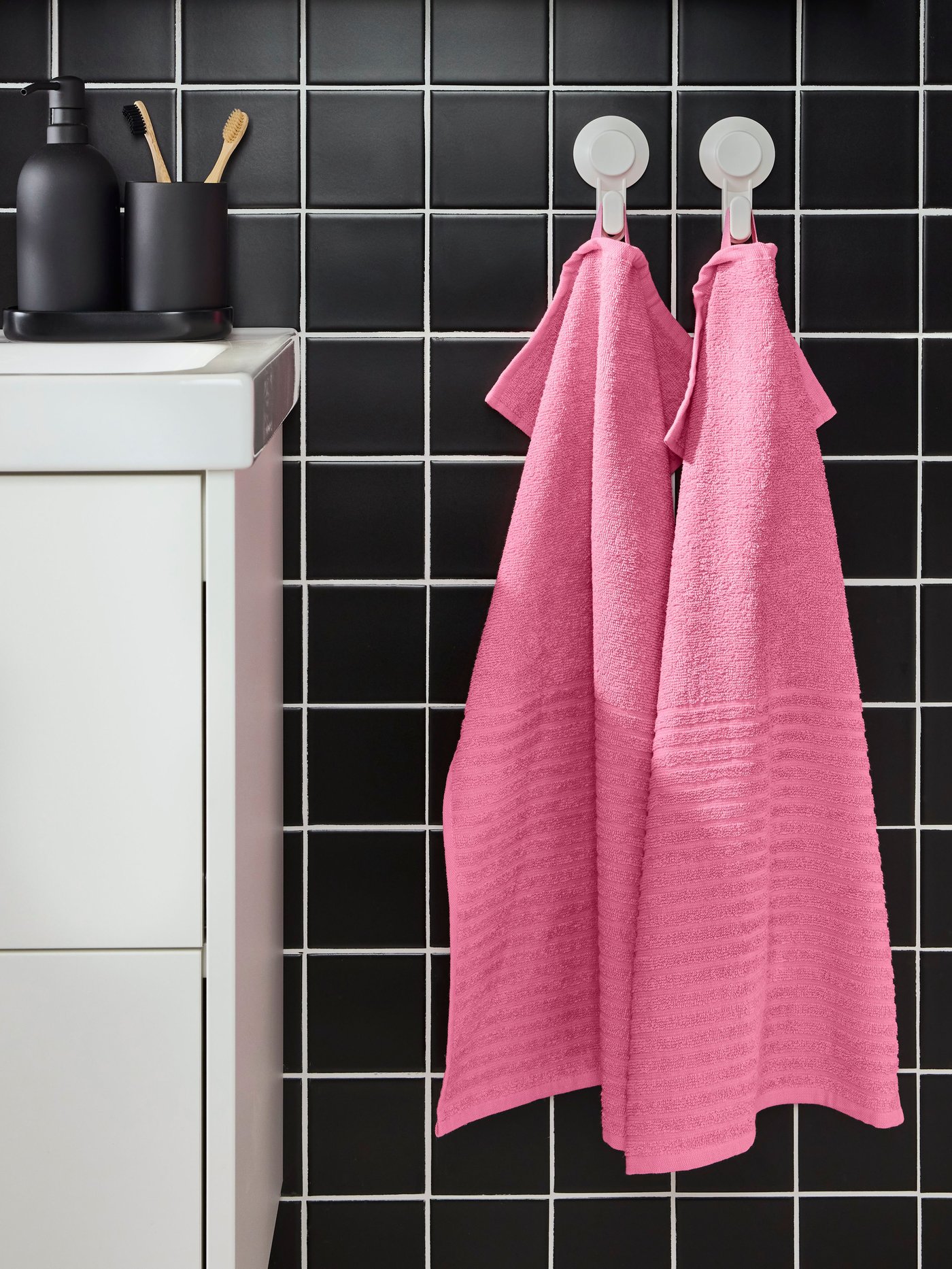 Zwei pinke VÅGSJÖN Handtücher an der Wand neben einem Waschtisch.