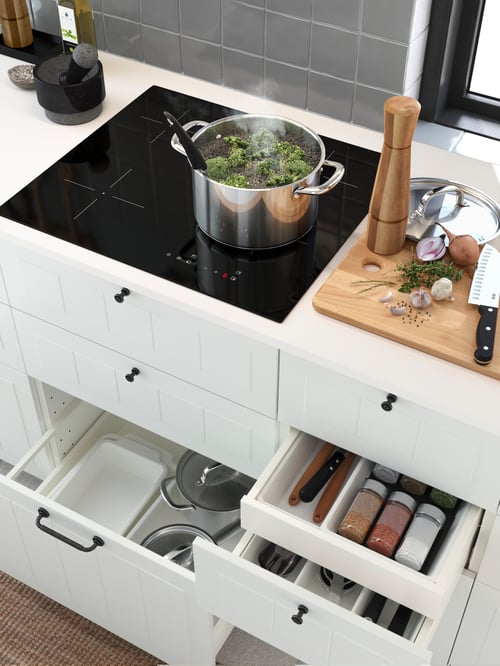 O bucătărie cu un vas IKEA 365+ cu capac lângă un tocător și o moară de condimente. O farfurie de cuptor este așezată într-un sertar.