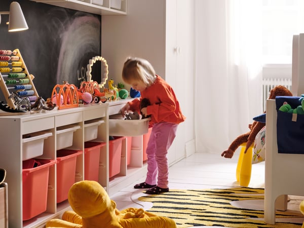 A children’s room with a long storage combination along the wall and a little girl looking for something in a drawer.