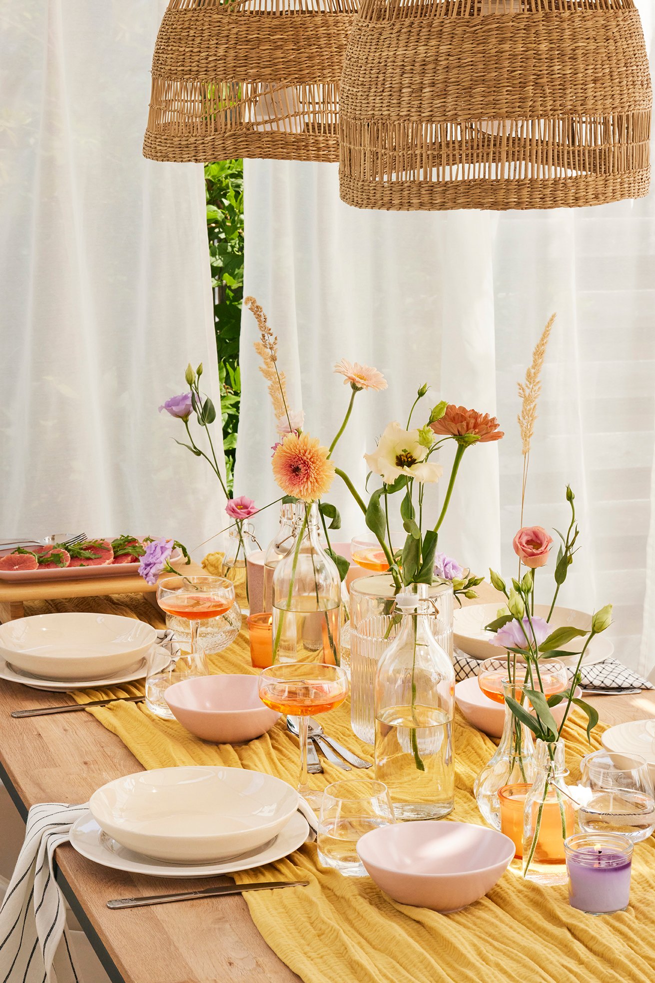 A cosy outdoor table setting with vases, flowers and two natural TORARED pendant lamps hanging above the table.