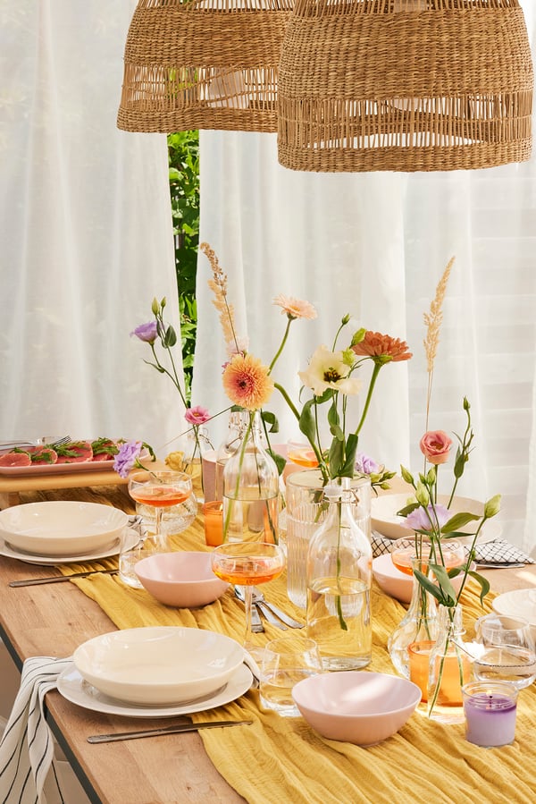 Vue d'une table de salle à manger dressée pour l'été avec beaucoup de fleurs dans différents vases